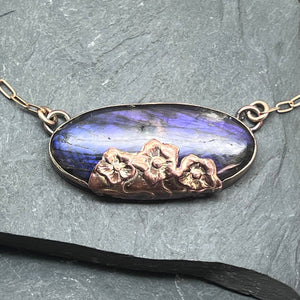 Necklace with a Labradorite pendant and copper floral elements on a stone surface